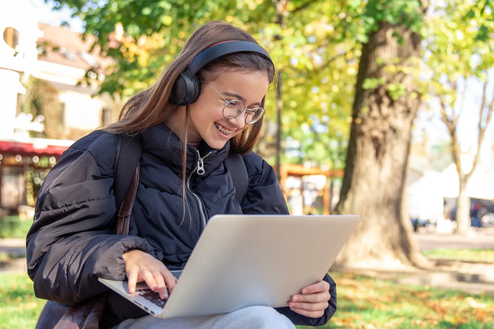 Teenage student with headphones using a laptop outdoors to work on a Cal State Apply application