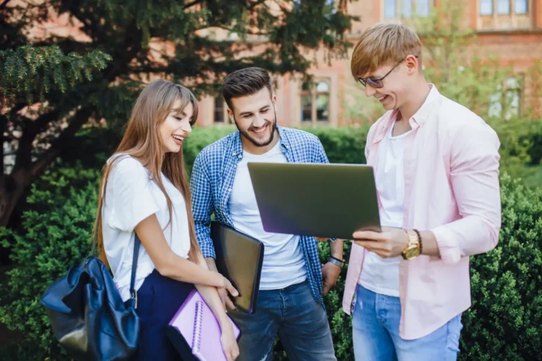 College students laughing over a laptop outside a campus building