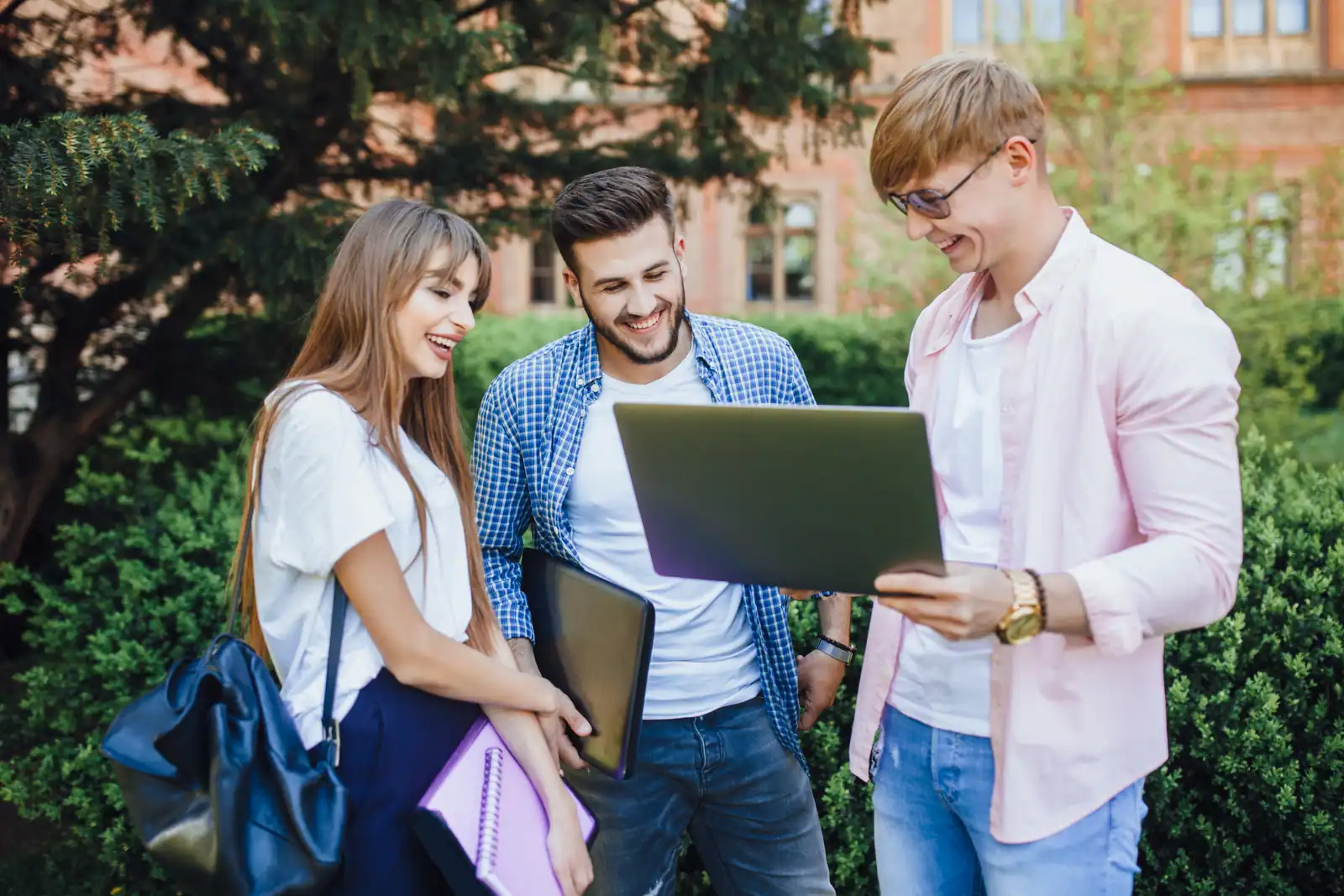 College students laughing over a laptop outside a campus building