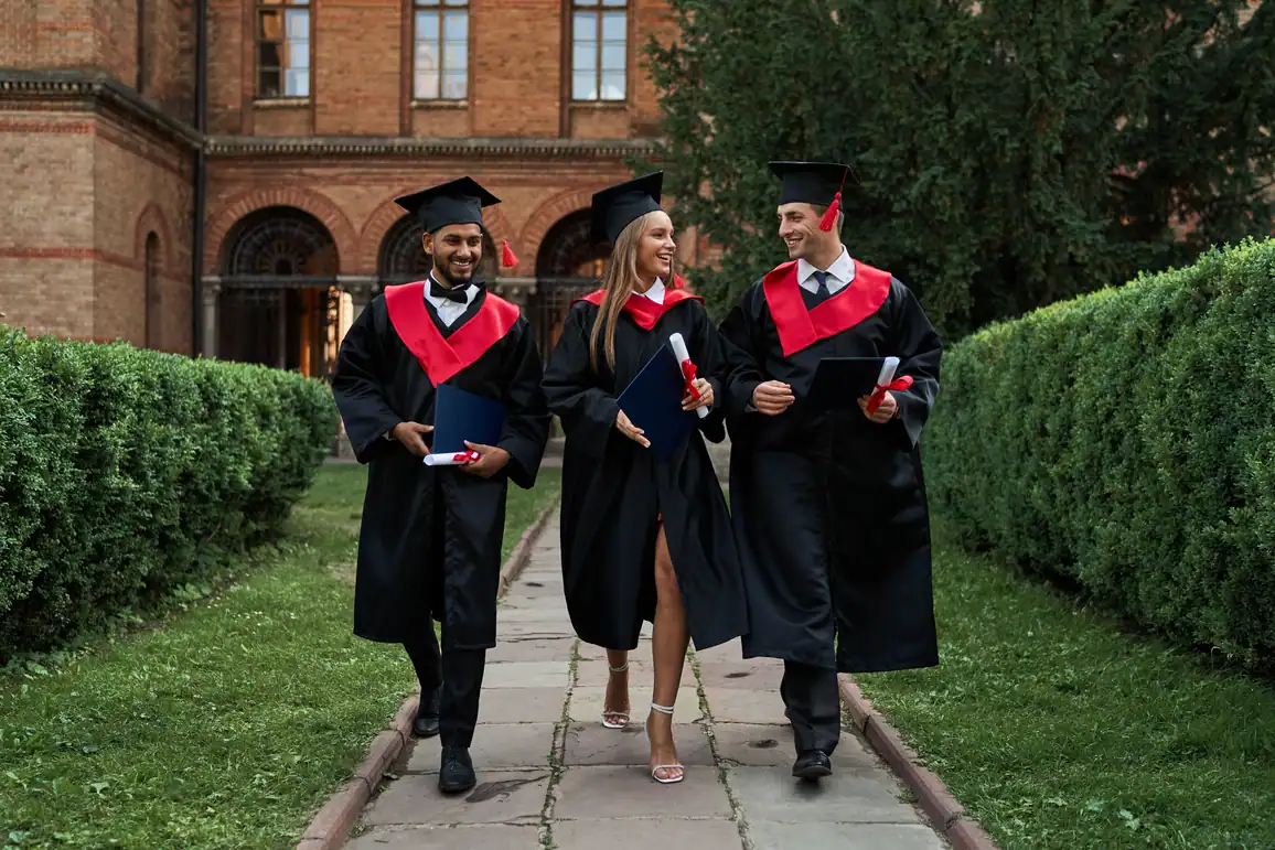 Three graduates in caps and gowns walking across a university campus