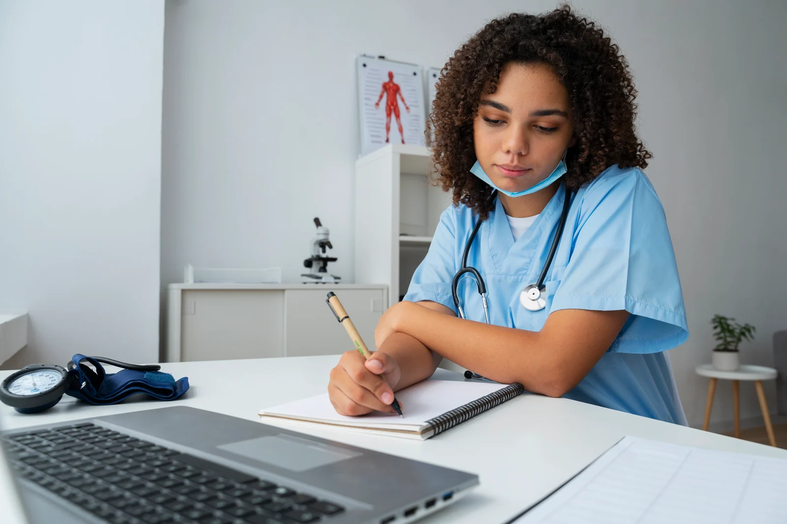 Nursing student in scrubs taking notes at a desk