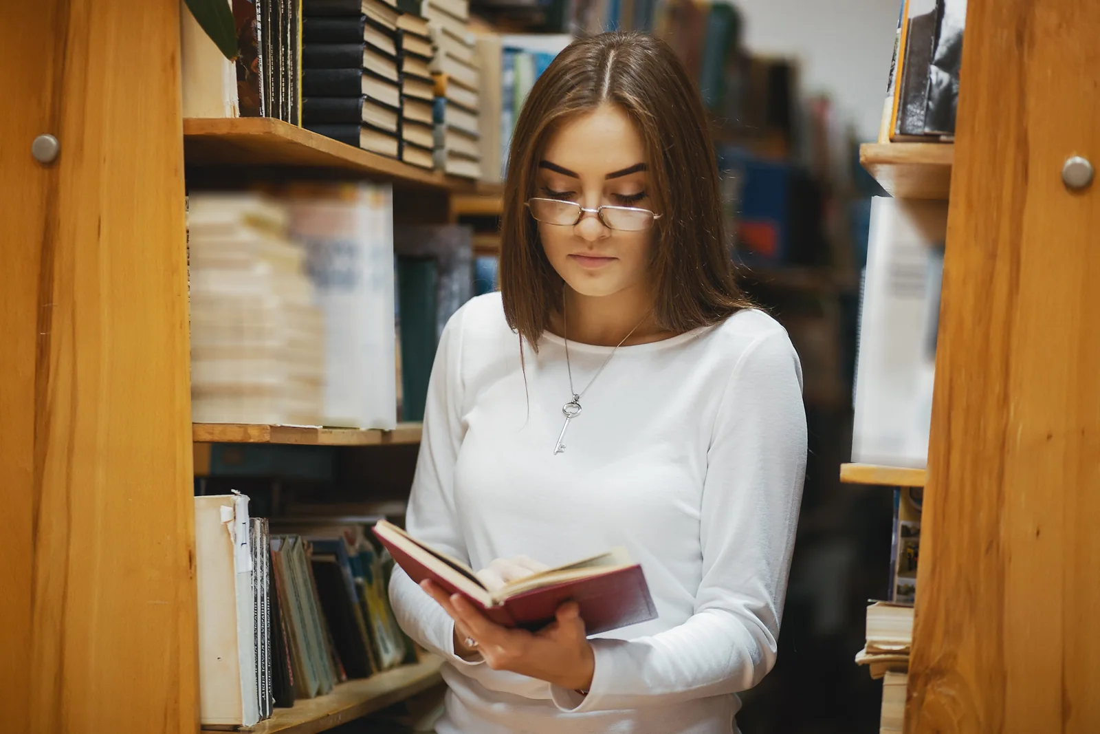 Female student reading a book between library shelves