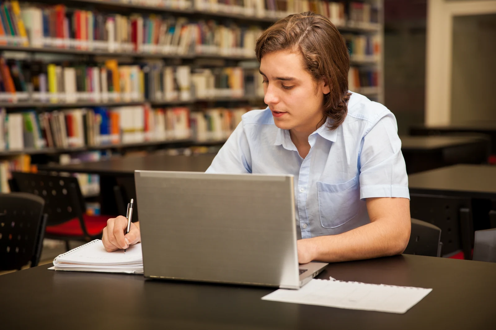 Student taking notes at a laptop in a library while working on a college application before the November deadline